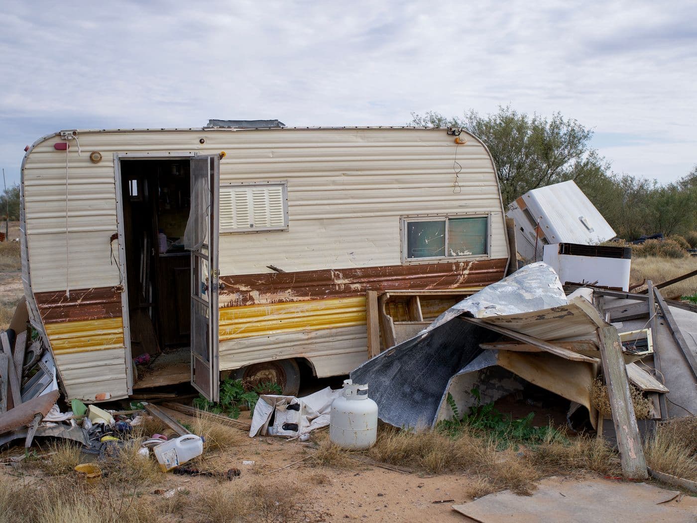 Old, damaged mobile home surrounded by debris